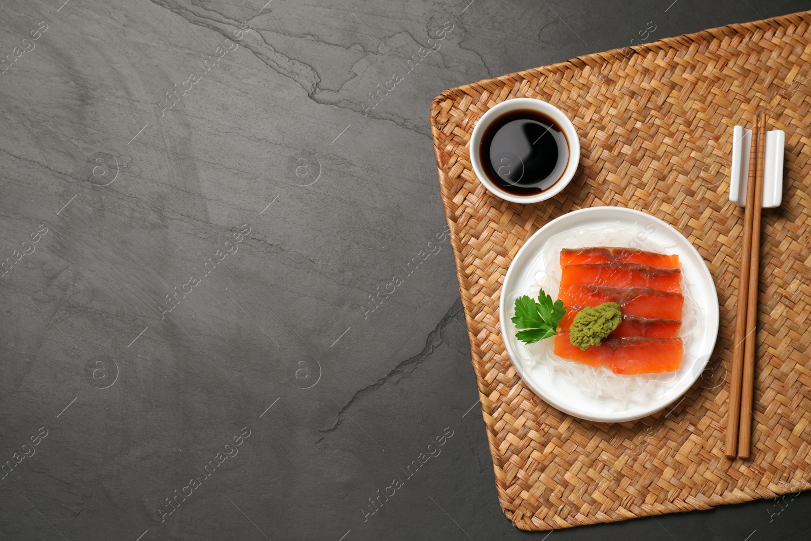Photo of Sashimi set (raw salmon slices) served with funchosa, parsley, vasabi and soy sauce on dark table, top view. Space for text