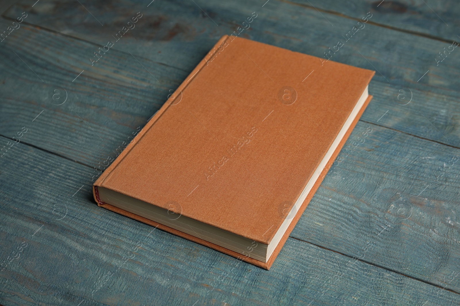 Photo of Hardcover book on light blue wooden table. Space for text