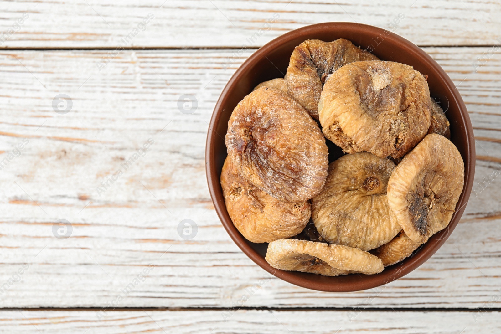 Photo of Bowl of dried figs on white wooden table, top view. Space for text