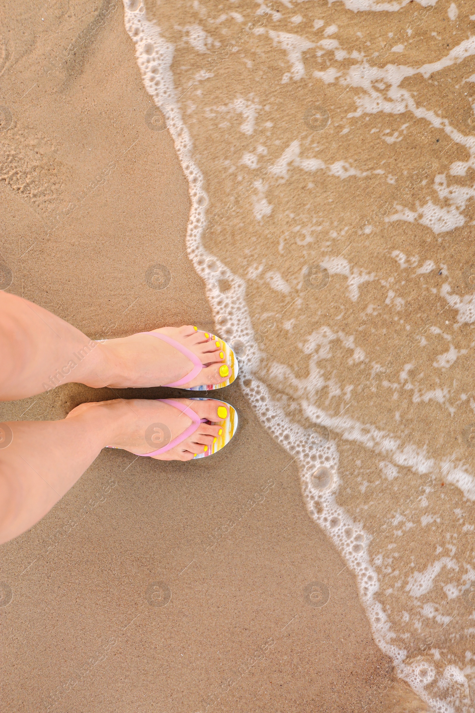 Photo of Top view of woman with stylish flip flops on sand near sea, space for text. Beach accessories