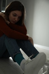 Photo of Sad young woman sitting on floor near grey wall indoors