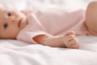 Photo of Cute little baby lying on white sheets, selective focus
