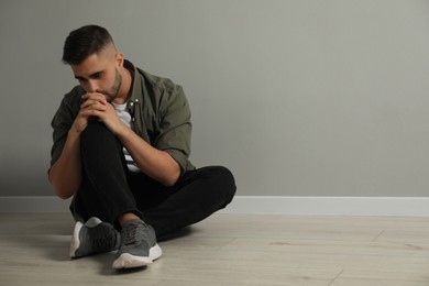 Photo of Sad man sitting on floor near light grey wall. Space for text