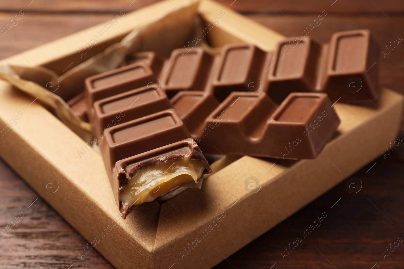 Photo of Cardboard box with tasty chocolate bars on wooden table, closeup