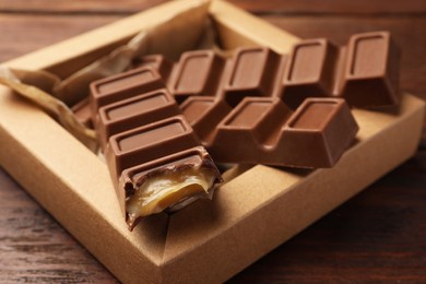 Cardboard box with tasty chocolate bars on wooden table, closeup