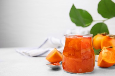 Photo of Jar of tasty persimmon jam, ingredients on white table. Space for text