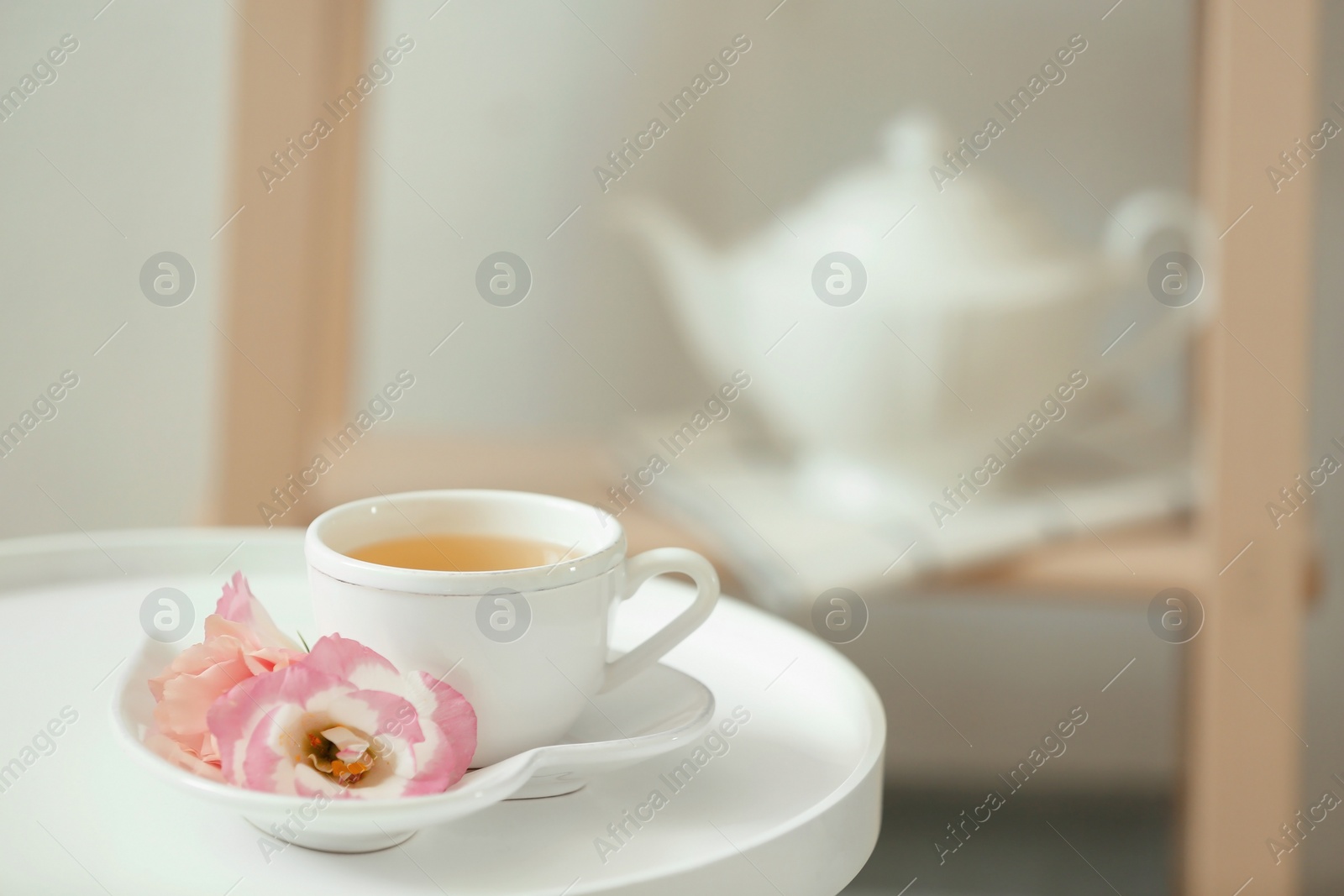 Photo of Cup of tea, saucer and flowers on table indoors