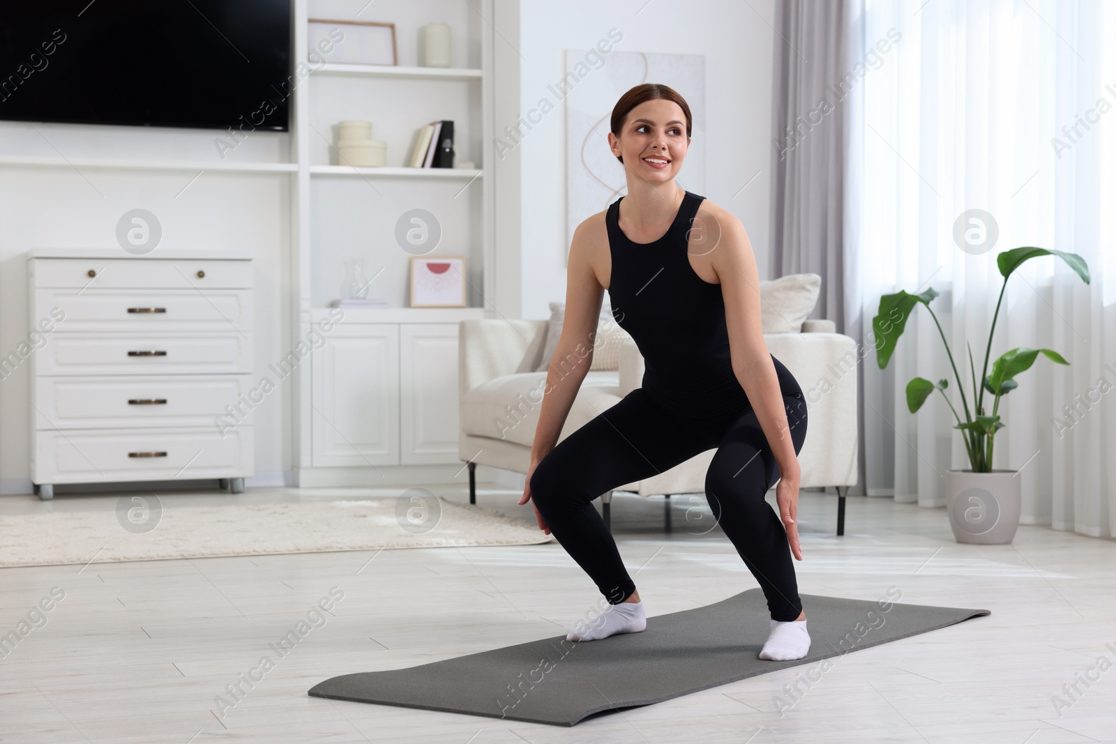 Photo of Morning exercise. Happy woman squatting at home, space for text