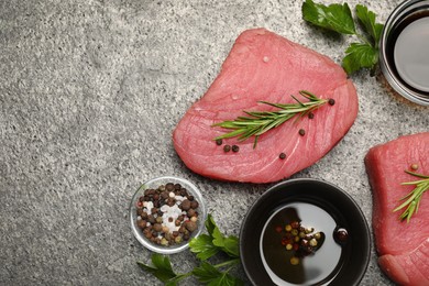 Photo of Raw tuna fillets with herbs and spices on gray table, flat lay. Space for text