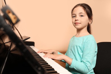 Photo of Cute little girl playing piano near beige wall. Music lesson