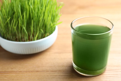 Glass of spirulina drink and wheatgrass on wooden table, closeup with space for text