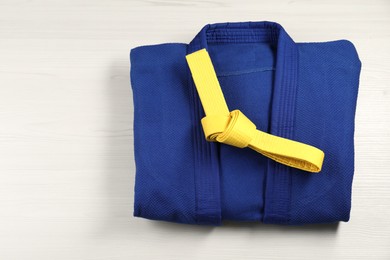 Yellow karate belt and blue kimono on wooden background, top view. Space for text