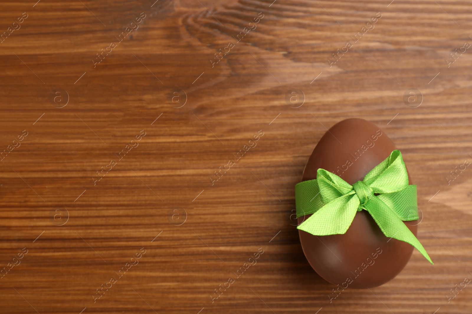 Photo of Sweet chocolate egg with green bow on wooden table, top view. Space for text