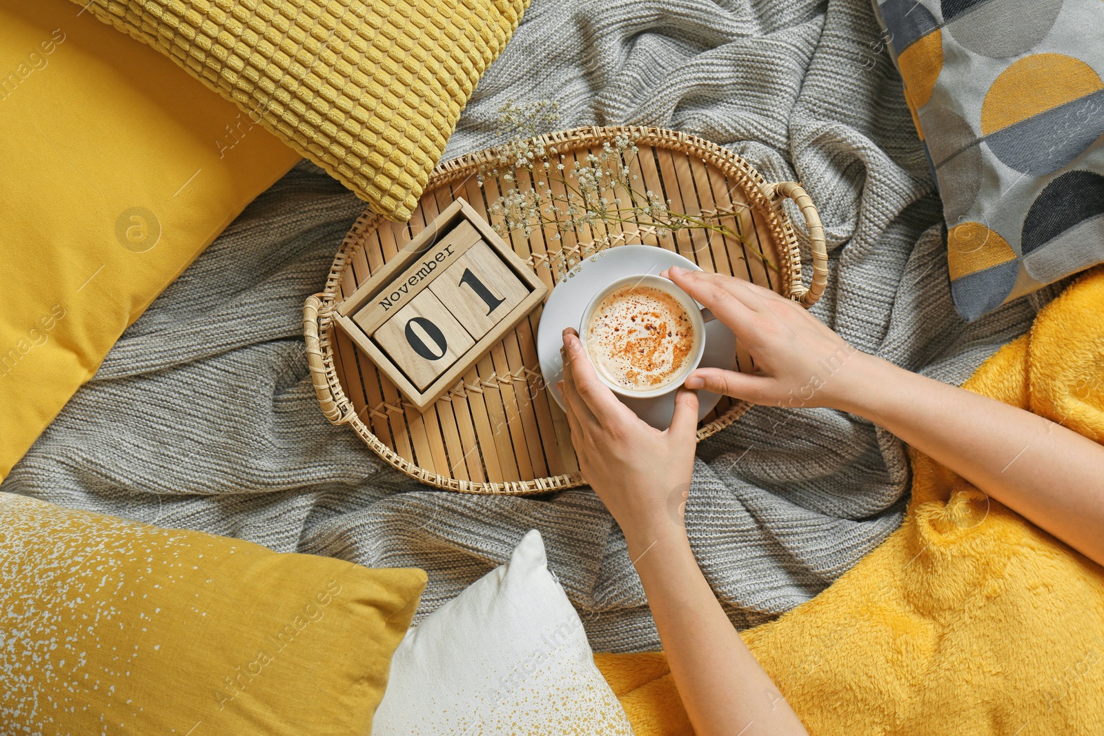 Photo of Woman holding cup of coffee while lying on bed with pillows and warm plaid, top view