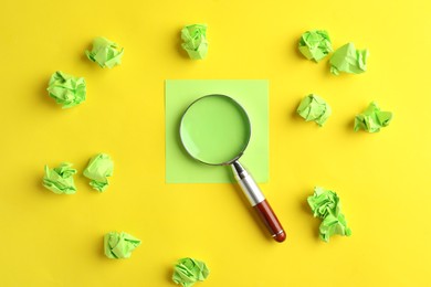 Magnifier glass, empty card and green crumpled paper sheets on yellow background, flat lay. Find keywords concept