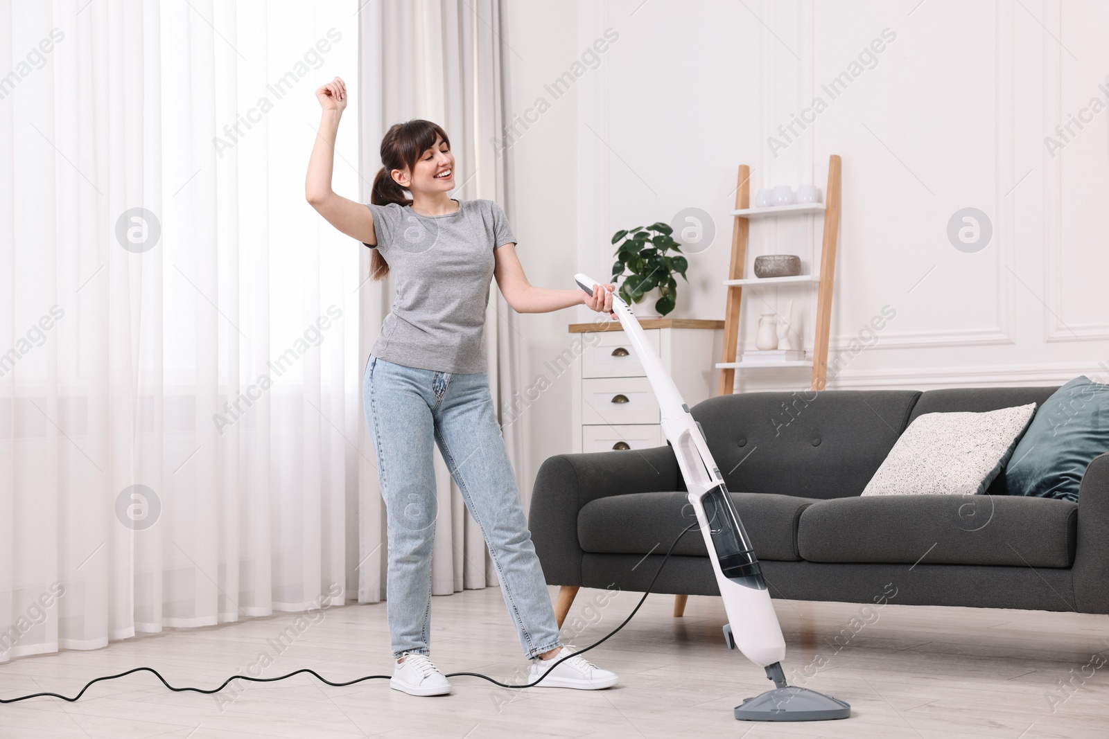 Photo of Happy young housewife cleaning floor with steam mop at home