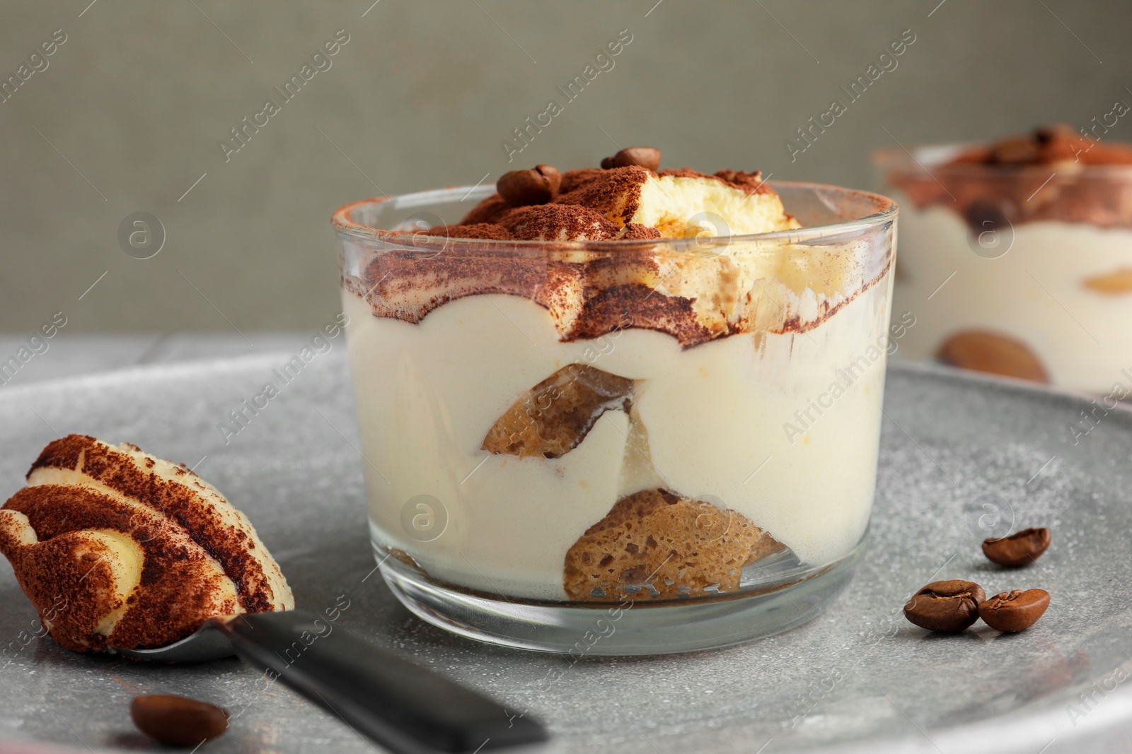 Photo of Delicious tiramisu in glass, coffee beans and spoon on table, closeup