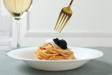 Eating tasty spaghetti with tomato sauce and black caviar at table, closeup. Exquisite presentation of pasta dish