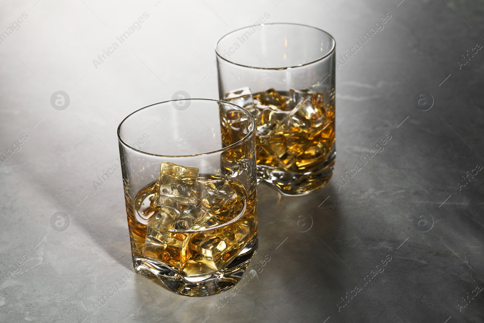 Photo of Whiskey with ice cubes in glasses on grey marble table