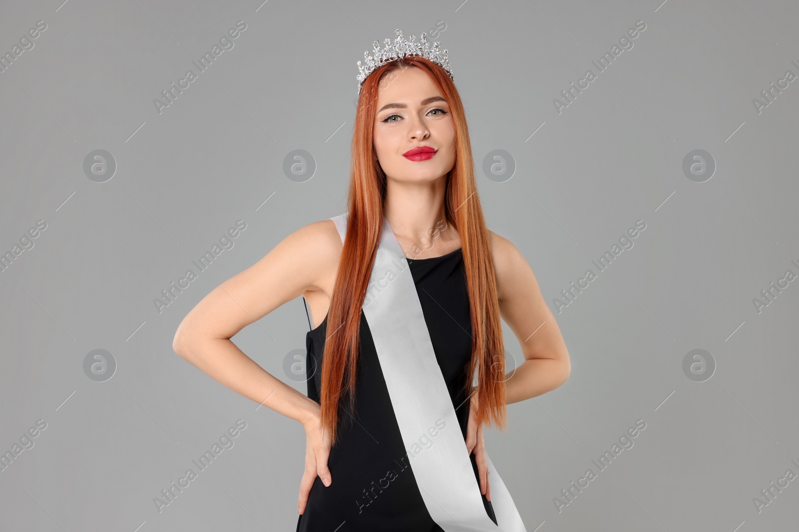 Photo of Beautiful young woman with tiara and ribbon in dress on light grey background. Beauty contest