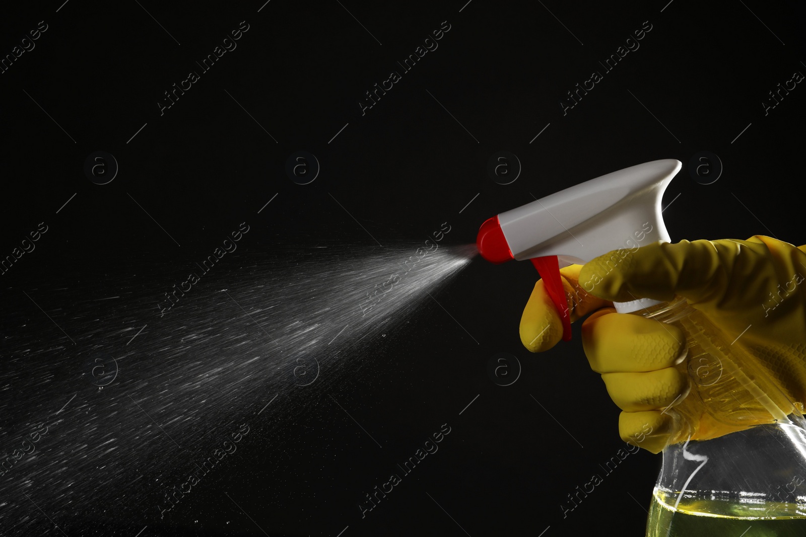 Photo of Woman spraying liquid from bottle on black background, closeup