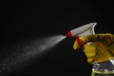 Photo of Woman spraying liquid from bottle on black background, closeup