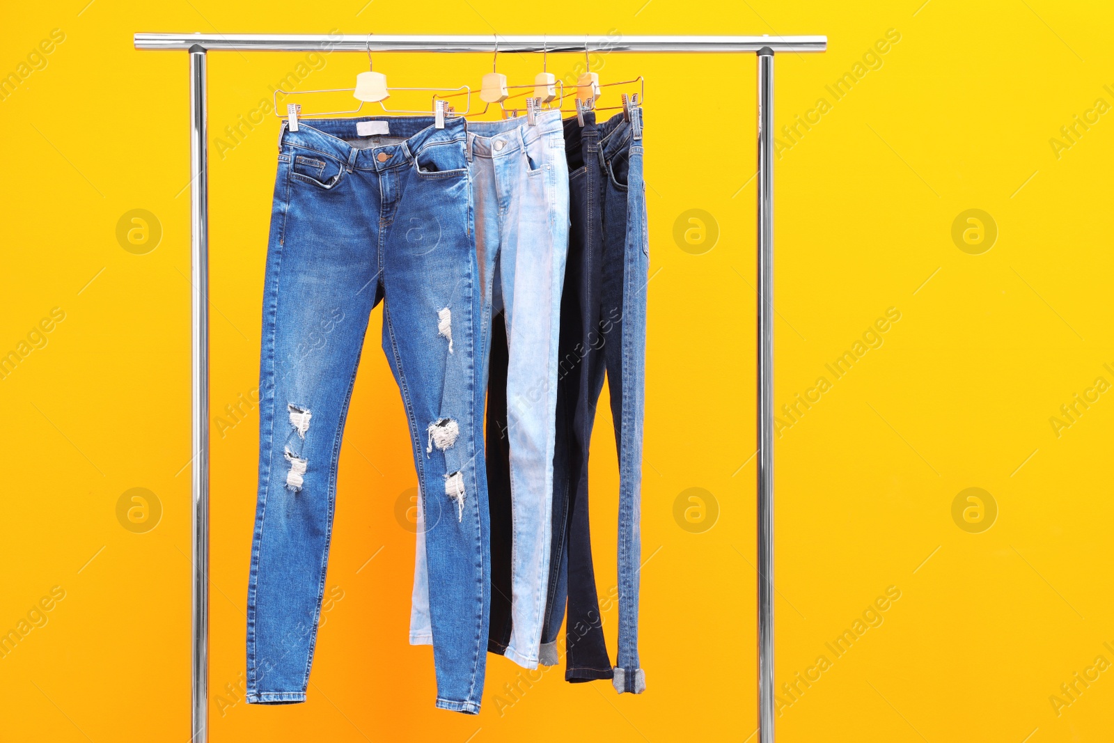 Photo of Rack with stylish jeans on color background