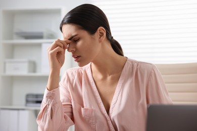Photo of Young woman suffering from headache at table in office