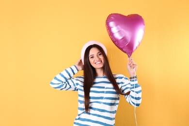 Portrait of young woman with heart shaped balloon on color background