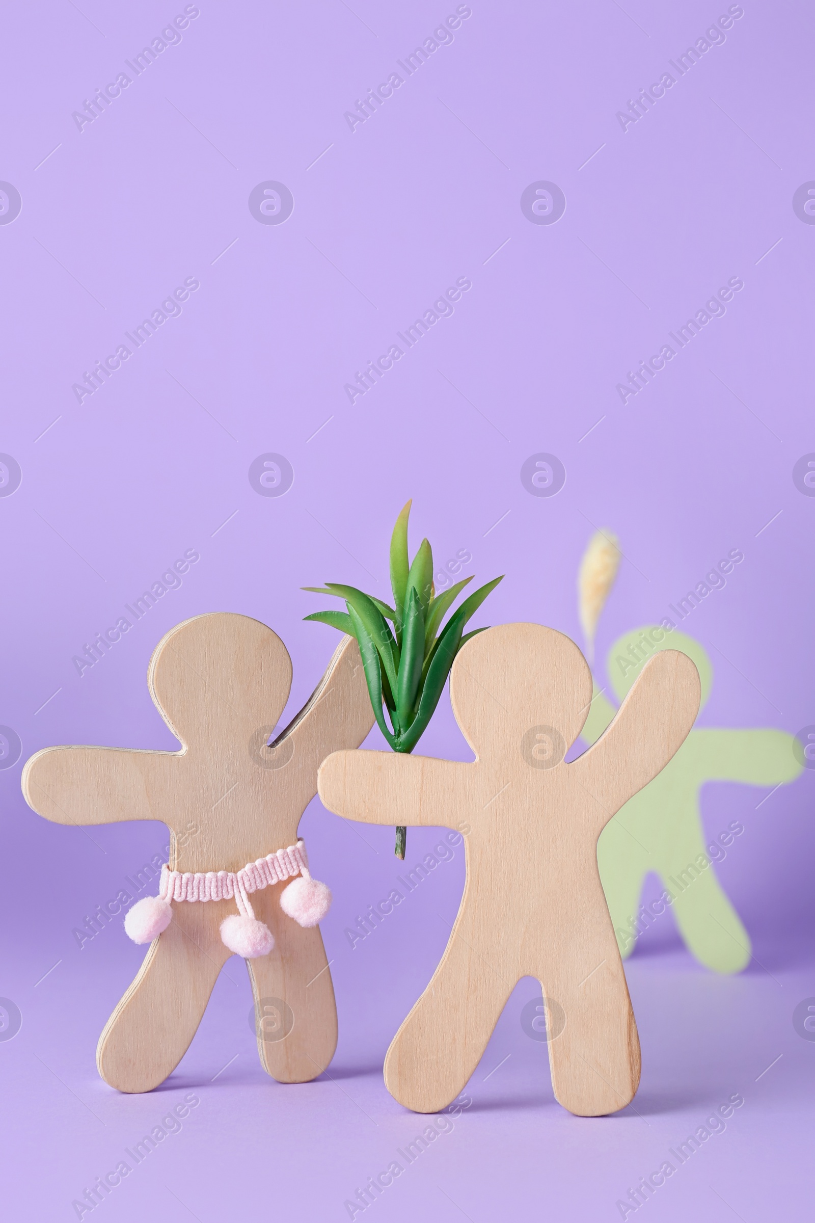 Photo of Wooden human figures fighting for attention of their beloved on lilac background. Jealousy concept