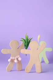 Photo of Wooden human figures fighting for attentiontheir beloved on lilac background. Jealousy concept