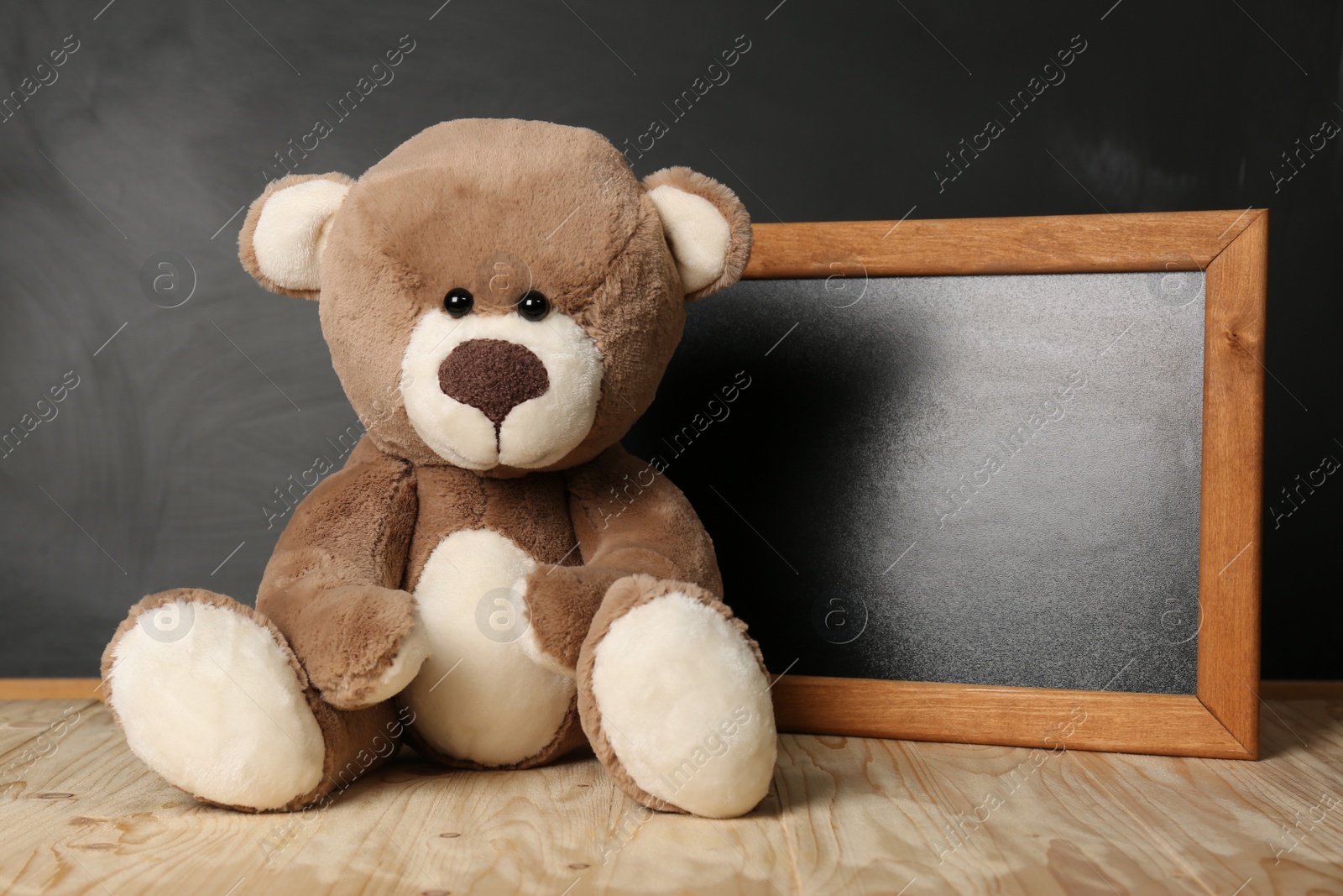 Photo of Teddy bear and small blackboard on wooden table. Space for text