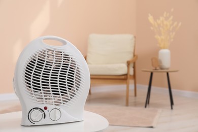 Photo of Compact electric fan heater on white table indoors, closeup. Space for text