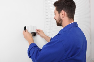 Photo of Technician installing home security alarm system on white wall indoors