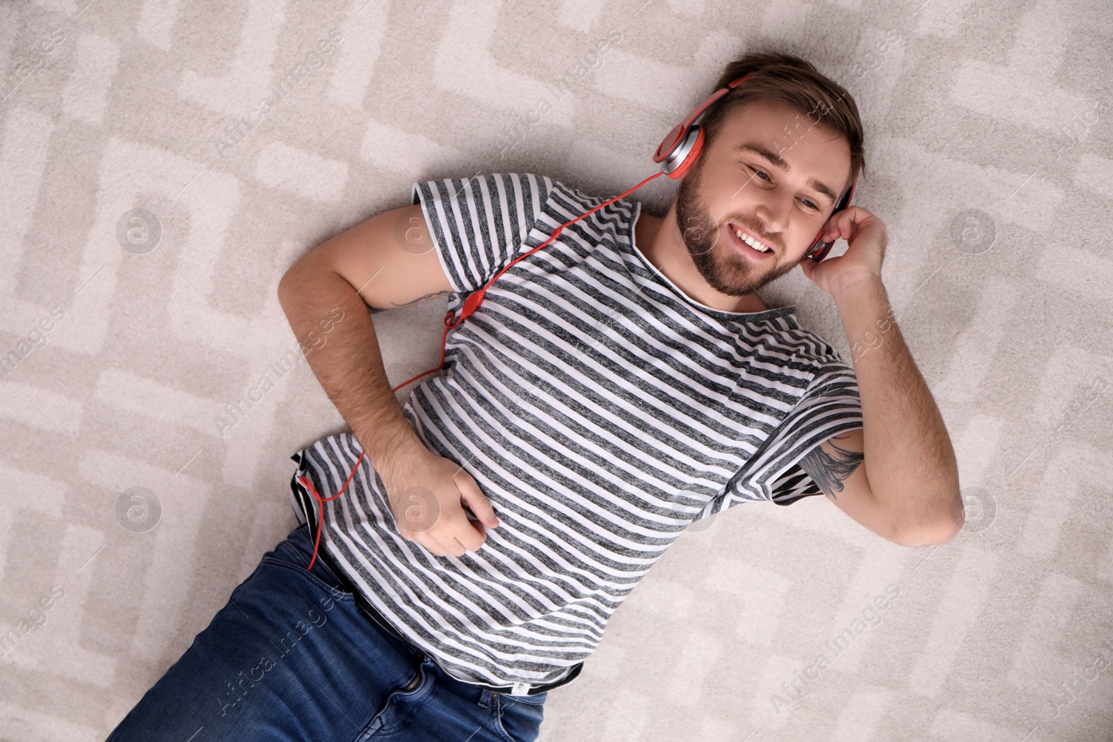 Photo of Young man in headphones enjoying music on floor, top view