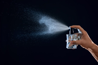 Photo of Young man spraying perfume on black background, closeup