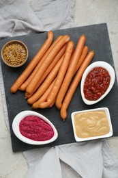 Delicious sausages, ketchup, mustard and horseradish on grey table, flat lay