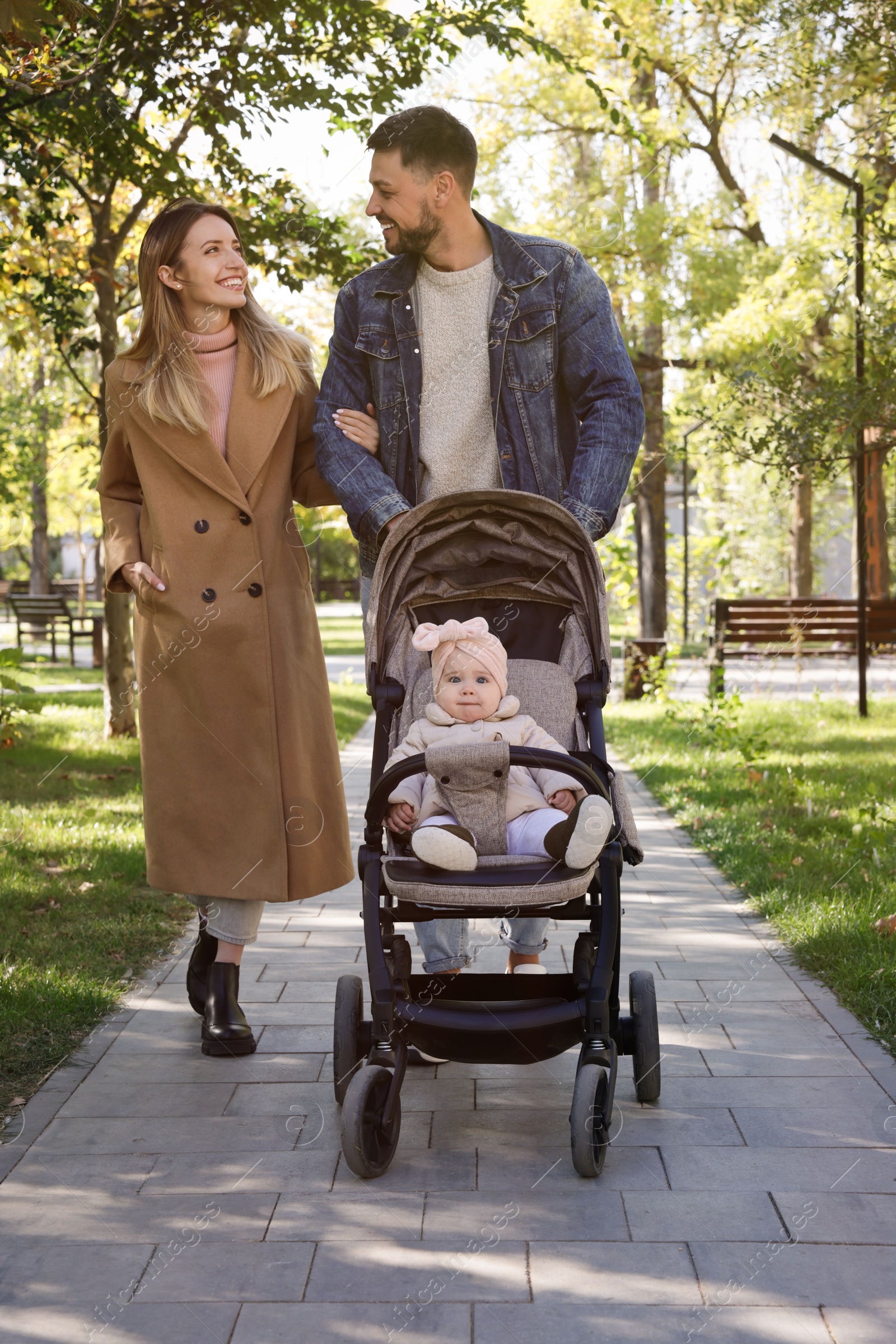 Photo of Happy parents walking with their baby in stroller at park on sunny day