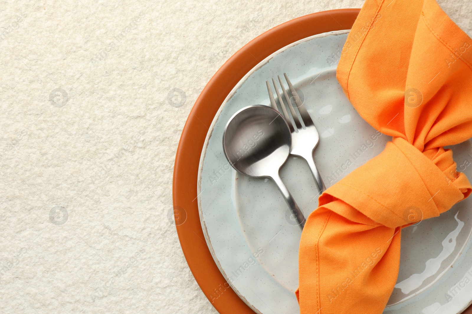 Photo of Stylish setting with cutlery, napkin and plates on light textured table, top view. Space for text