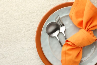 Photo of Stylish setting with cutlery, napkin and plates on light textured table, top view. Space for text