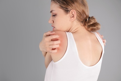 Photo of Woman scratching shoulder on grey background. Allergy symptoms