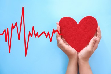 Image of Young woman holding red heart on light blue background, top view