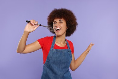 Photo of Happy young woman with whisk singing on purple background