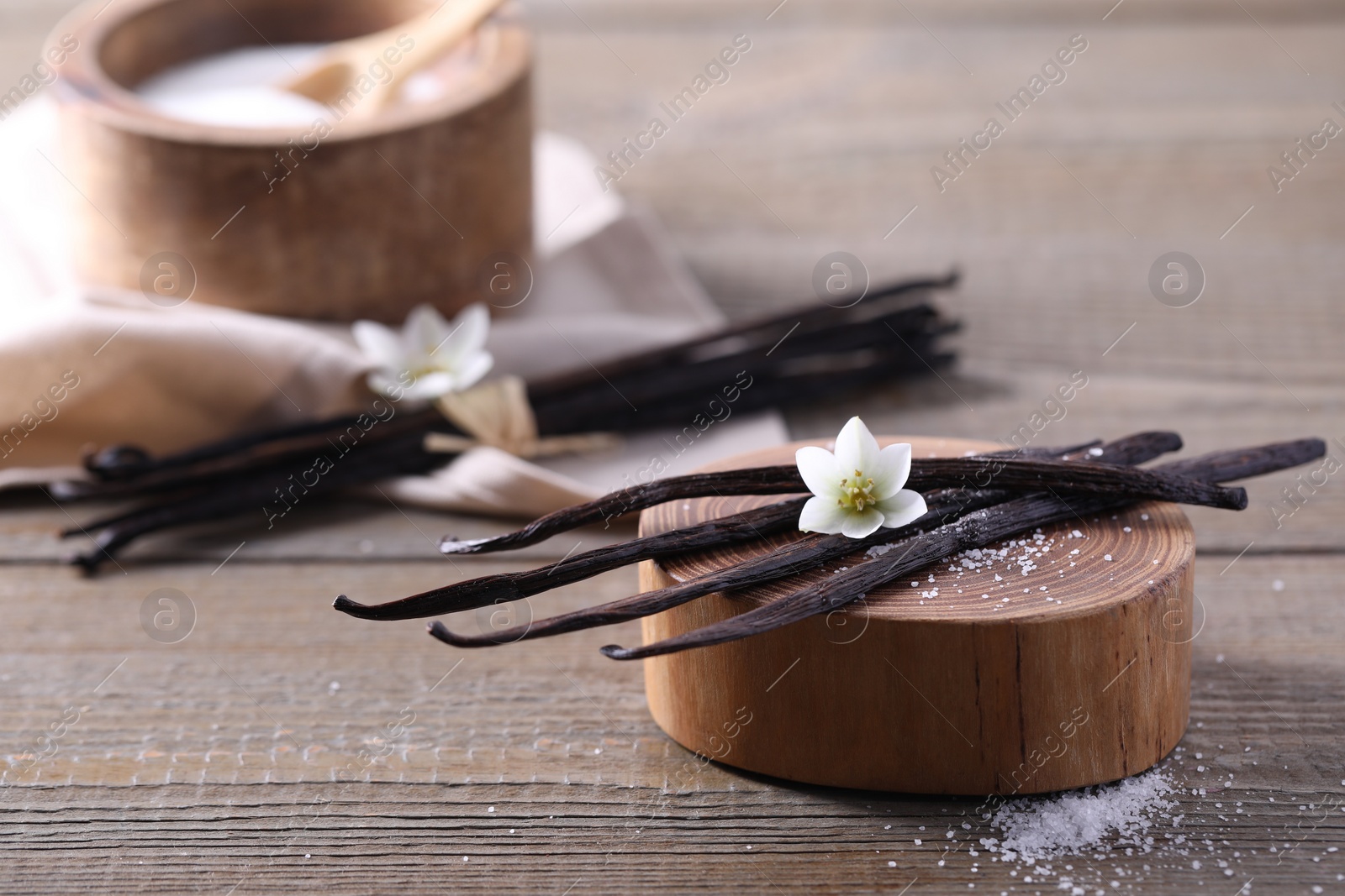 Photo of Vanilla pods, flower and sugar in bowl on wooden table, closeup