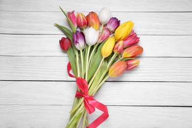 Bouquet of beautiful colorful tulip flowers tied with red ribbon on white wooden table, top view