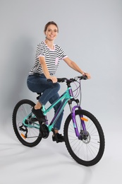 Photo of Happy young woman riding bicycle on grey background