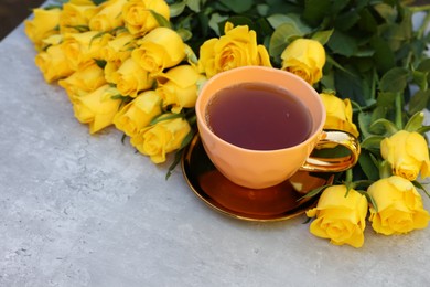 Cup of tea and beautiful yellow roses on light table, space for text