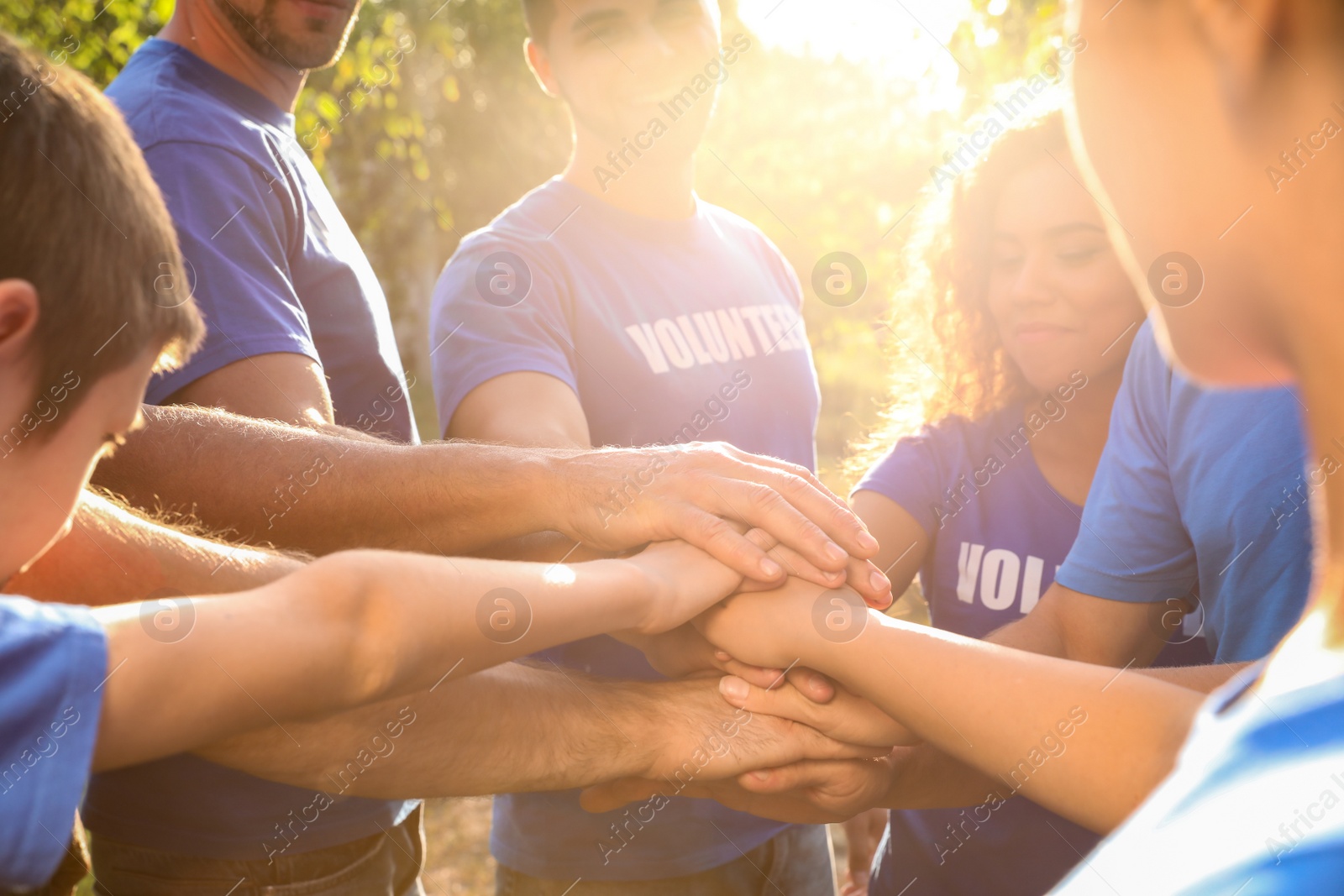 Photo of Group of volunteers joining hands together outdoors on sunny day