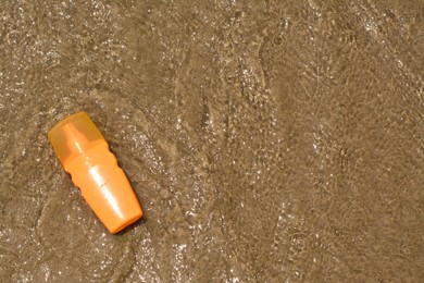 Photo of Bottle with sun protection spray on seashore, top view. Space for text