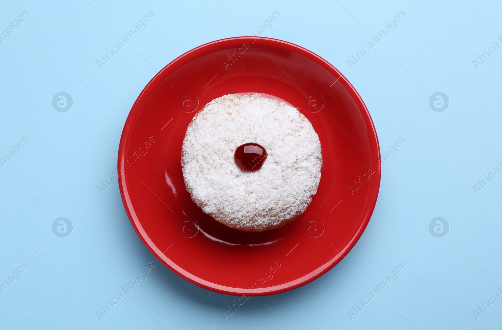 Photo of Hanukkah donut with jelly and powdered sugar on light blue background, top view